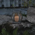 Solarny lampion LED ustawiony na kamiennym murku w ogrodzie, emitujący ciepłe światło po zmroku.