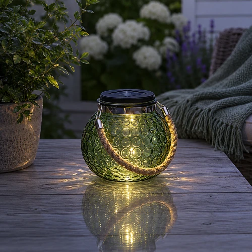 Zielony lampion solarny LED z jutowym uchwytem na drewnianym stole w ogrodzie o zmierzchu.