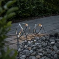 Dwie solarne kule dekoracyjne LED ustawione przy kamiennej rabacie w ogrodzie. Metalowe obręcze tworzą geometryczne formy, a subtelne światło podkreśla ich kształt i rzuca delikatne cienie na nawierzchnię.