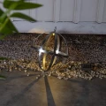 Metalowa kula solarna z podświetleniem LED umieszczona na nawierzchni przy elewacji budynku. Ażurowa konstrukcja tworzy na podłożu wyraźne cienie podkreślające geometryczny charakter dekoracji.