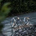 Dwie metalowe kule solarne LED ustawione przy kamiennej rabacie ogrodowej. Światło wewnątrz obręczy akcentuje przestrzenną formę dekoracji i tworzy efektowne refleksy na otaczającej nawierzchni.