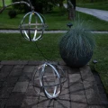 Dwie metalowe kule solarne LED wykorzystane jako dekoracja tarasu i ogrodu. Jedna kula ustawiona jest na kostce brukowej, druga zawieszona nad nią, a delikatne światło podkreśla geometryczny kształt obu ozdób.