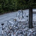 Dwie solarne kule dekoracyjne LED umieszczone w ogrodowej aranżacji z kamieni ozdobnych. Jedna ozdoba stoi na rabacie, druga została zawieszona, tworząc efekt przestrzennej kompozycji świetlnej.