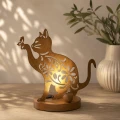 Solarny kot LED w kolorze rdzawego brązu z ażurowym wzorem kwiatowym. Dekoracja ustawiona na okrągłej podstawie emituje delikatne światło przez wycinane ornamenty, a na uniesionej łapie widoczny jest motyl.