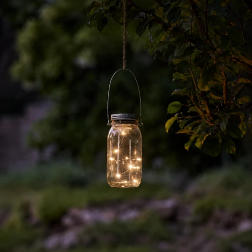 Solarna lampa LED w szklanym słoiku zawieszona na uchwycie. Delikatne punkty świetlne umieszczone wewnątrz tworzą ciepły blask, nadając ogrodowi, tarasowi lub balkonowi przytulny i dekoracyjny charakter po zmroku.
