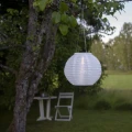 Wiszący lampion solarny LED zawieszony wśród gałęzi drzewa. Jasny klosz subtelnie rozprasza światło, tworząc nastrojowy akcent w przestrzeni ogrodowej.