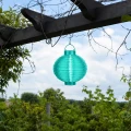 Niebieski lampion solarny LED zawieszony pod pergolą wśród zielonych pnączy. Okrągła dekoracja ogrodowa dodaje przestrzeni koloru i subtelnego oświetlenia po zmroku.