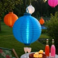 Niebieski lampion solarny LED zawieszony w ogrodzie podczas letniego spotkania. Kolorowa dekoracja świetlna tworzy przyjemny klimat na tarasie i w strefie wypoczynku.