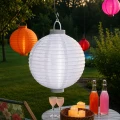 Biały lampion solarny LED zawieszony nad ogrodowym stolikiem z dekoracjami. Delikatne oświetlenie tworzy przytulny nastrój podczas wieczornego wypoczynku na tarasie.