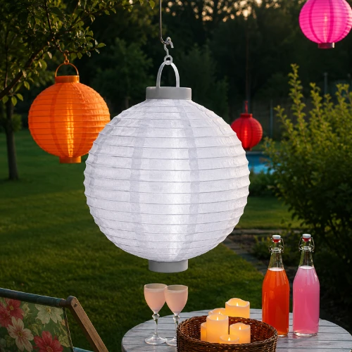 Biały lampion solarny LED zawieszony nad ogrodowym stolikiem z dekoracjami. Delikatne oświetlenie tworzy przytulny nastrój podczas wieczornego wypoczynku na tarasie.