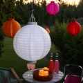 Elegancki biały lampion solarny LED zawieszony wśród kolorowych lampionów ogrodowych. Dekoracja świetlna podkreśla klimat letnich spotkań na świeżym powietrzu.