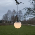 Zawieszona lampa solarna w formie podświetlanej kuli nad rozległym trawnikiem. Delikatne światło podkreśla spokojny charakter ogrodowej aranżacji o zmroku.