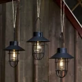 Trzy wiszące lampy solarne z ciepłym światłem rozmieszczone na różnych wysokościach na tle drewnianej ściany, tworzą dekoracyjną aranżację świetlną.