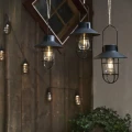 Trzy wiszące lampy solarne z charakterystycznym daszkiem i ozdobną osłoną żarówki tworzą klimatyczną aranżację na tle drewnianej ściany.