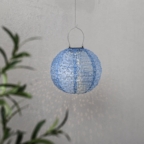 Ażurowy lampion solarny LED w kształcie kuli zawieszony na cienkiej lince. Delikatne światło tworzy dekoracyjne refleksy na jasnej ścianie.