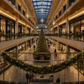 Girlandy udekorowane oświetleniem zdobią szklane balustrady galerii handlowej, a w centralnej części wnętrza ustawiono wysoką choinkę z dekoracyjnym oświetleniem.