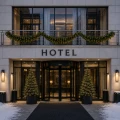 Girlanda LED z zielonego igliwia zawieszona na balustradzie nad wejściem do hotelu. Poniżej znajdują się obrotowe drzwi, a po obu stronach wejścia ustawiono podświetlone choinki w donicach.