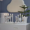 Dwa świeczniki LED z motywami Pippi Pończoszanki ustawione na białej komodzie. W tle znajdują się roślina w doniczce oraz dekoracja ścienna w kształcie chmurki.
