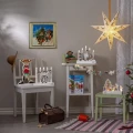Świąteczna aranżacja z kilkoma świecznikami LED z motywami Pippi Pończoszanki ustawionymi na stolikach i krześle. Całość uzupełniają papierowa gwiazda, choinka oraz świąteczne dekoracje.