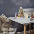Świąteczna scenka LED z motywami Pippi Pończoszanki ustawiona na dziecięcym stoliku obok pluszowego misia. Kolorowe postacie i podświetlana choinka tworzą ciepłą, świąteczną dekorację.