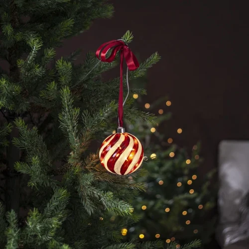 Szklana bombka LED z czerwonym spiralnym wzorem zawieszona na gałązce choinki na czerwonej satynowej wstążce. W tle widać subtelnie rozmyte świąteczne światełka.