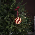 Szklana bombka LED z czerwonym spiralnym wzorem zawieszona na gałązce choinki na czerwonej satynowej wstążce. Ciemne tło podkreśla ciepłe światło dekoracji.