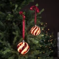 Dwie szklane bombki LED z czerwonym spiralnym wzorem zawieszone na gałązkach choinki na czerwonych satynowych wstążkach. Ciepłe światło dekoracji tworzy przytulny świąteczny klimat.