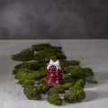 Czerwony ceramiczny dzwonek LED z białą kokardą tworzy świąteczną dekorację wyeksponowaną na zielonym mchu.