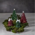 Zielony i czerwony ceramiczny świecznik w kształcie dzwonka ustawiono przed dwiema dekoracyjnymi choinkami z ceramiki. Wycięcia w kształcie gwiazdek subtelnie przepuszczają światło, a całość uzupełnia dekoracja z naturalnego mchu.