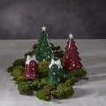 Świąteczna kompozycja z ceramicznymi choinkami i dzwonkami w czerwonym oraz zielonym kolorze, ustawionymi na mchu. Dekoracje mają błyszczące wykończenie i ozdobne wycięcia.