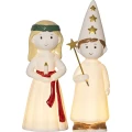Świecące figurki na białym tle przedstawiają postać z wysoką czapką ozdobioną złotymi gwiazdami oraz postać z wiankiem na głowie i świecą w dłoniach.