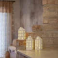 W przytulnym wnętrzu ustawiono trzy podświetlane ceramiczne domki w białym kolorze. Światło widoczne w oknach podkreśla detale fasad.