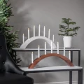 Biały i drewniany świecznik łukowy z siedmioma smukłymi świecami LED, ustawione na dwóch stolikach w eleganckiej aranżacji z zielonymi gałązkami.