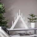 Biały świecznik LED o trójkątnej formie z siedmioma świecami ustawiony na konsoli, w spokojnym wnętrzu z choinką i zieloną gałązką w donicy.
