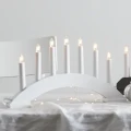 Zbliżenie białego świecznika w formie łuku z siedmioma białymi świecami, ustawionego na jasnym stole z delikatnymi lampkami.
