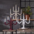 Biały, czerwony i beżowy świecznik z pięcioma białymi świecami, wyeksponowane na różnych poziomach w aranżacji z zielonymi gałązkami i szyszkami.