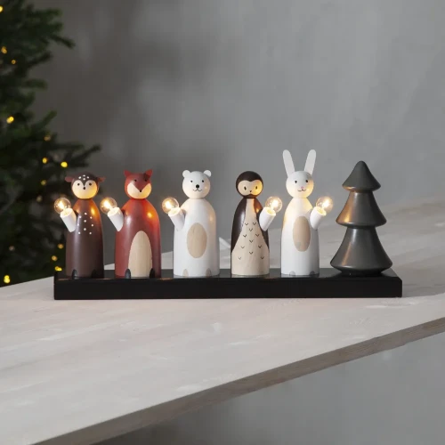 Dekoracyjny świecznik z figurkami leśnych zwierząt, jelonka, lisa, niedźwiedzia, sowy i królika, ustawiony na jasnym stole obok choinki.