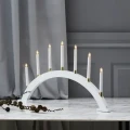 Łukowy biały świecznik z siedmioma punktami świetlnymi, ustawiony na jasnym blacie w stonowanej aranżacji z szarym tłem.
