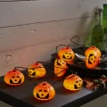 Łańcuch świetlny z podświetlanymi dyniami ułożony na ciemnym blacie obok naczyń i dodatków w halloweenowej aranżacji.