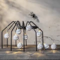 Łańcuch świetlny z podświetlanymi białymi dyniami rozwieszony na metalowej dekoracji w aranżacji Halloween z motywem pająka w tle.