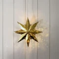 Wisząca gwiazda świetlna w kolorze mosiądzu z perforowanym wzorem, zawieszona na jasnej ścianie i tworząca dekoracyjne refleksy świetlne.