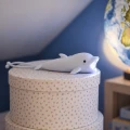 Na ozdobnym pudełku ustawiona niebieska latarka delfin z włączonym światłem, pokazana w dziecięcej aranżacji z globusem.
