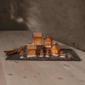 Piernikowa wioska z czterech rozświetlonych domków o różnych kształtach, ozdobionych białymi ornamentami, ustawiona na ciemnej tacy w towarzystwie małych figurek świątecznych i lasek cynamonu.