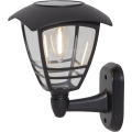 Solarna lampa ścienna LED w stylu latarni, z dekoracyjną żarówką i czarną obudową, przeznaczona do montażu na elewacji.