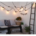 Girlanda ogrodowa z żarówkami A60 LED 2,3W 2100K Soft Glow zawieszona na czarnym przewodzie w pomieszczeniu. Żarówki w przezroczystych bańkach emitują ciepłe, miękkie światło, tworząc nastrojową iluminację.