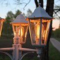 Ozdobna latarnia ogrodowa z dekoracyjnymi żarówkami LED filament świecącymi ciepłym światłem przy drodze o zachodzie słońca.