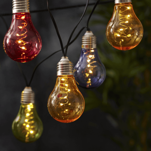 Kolorowa girlanda solarna LED z barwionymi żarówkami zawieszona w ogrodzie. Czerwone, żółte, zielone i niebieskie klosze z mikro diodami LED tworzą dekoracyjne, ciepłe światło po zmroku.