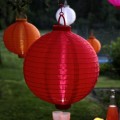 Czerwony lampion solarny LED zawieszony w ogrodzie. Kolorowa dekoracja świetlna tworzy przyjemny nastrój na tarasie, balkonie lub w altanie.