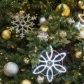 Fragment udekorowanej choinki z podświetlaną śnieżynką LED, błyszczącą srebrną śnieżynką oraz złotymi, srebrnymi i lustrzanymi bombkami wśród gęstych zielonych gałązek i ciepłych światełek.