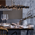 Lampki LED 180 diod 12m, oplatające gałąź dekoracyjną nad stołem, tworzące przytulne światło o ciepłej barwie 3000K.